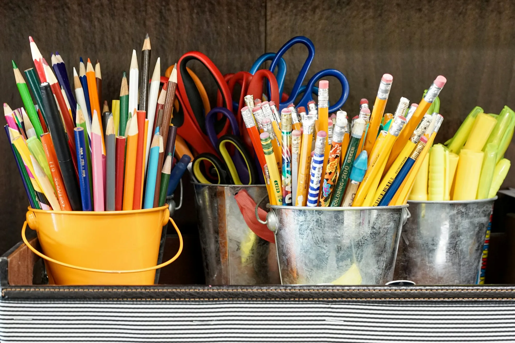 Colored pencils, pens and scissors in metal buckets